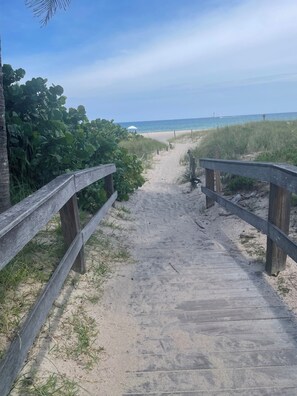 Ein Holzsteg führt zu einem Strand mit freiem Blick auf das Meer.