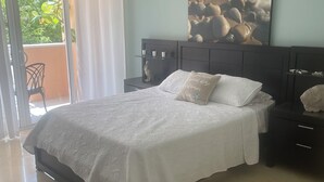 Quarto com cama, mesa de cabeceira, prateleira na parede e porta de vidro deslizante para área externa.