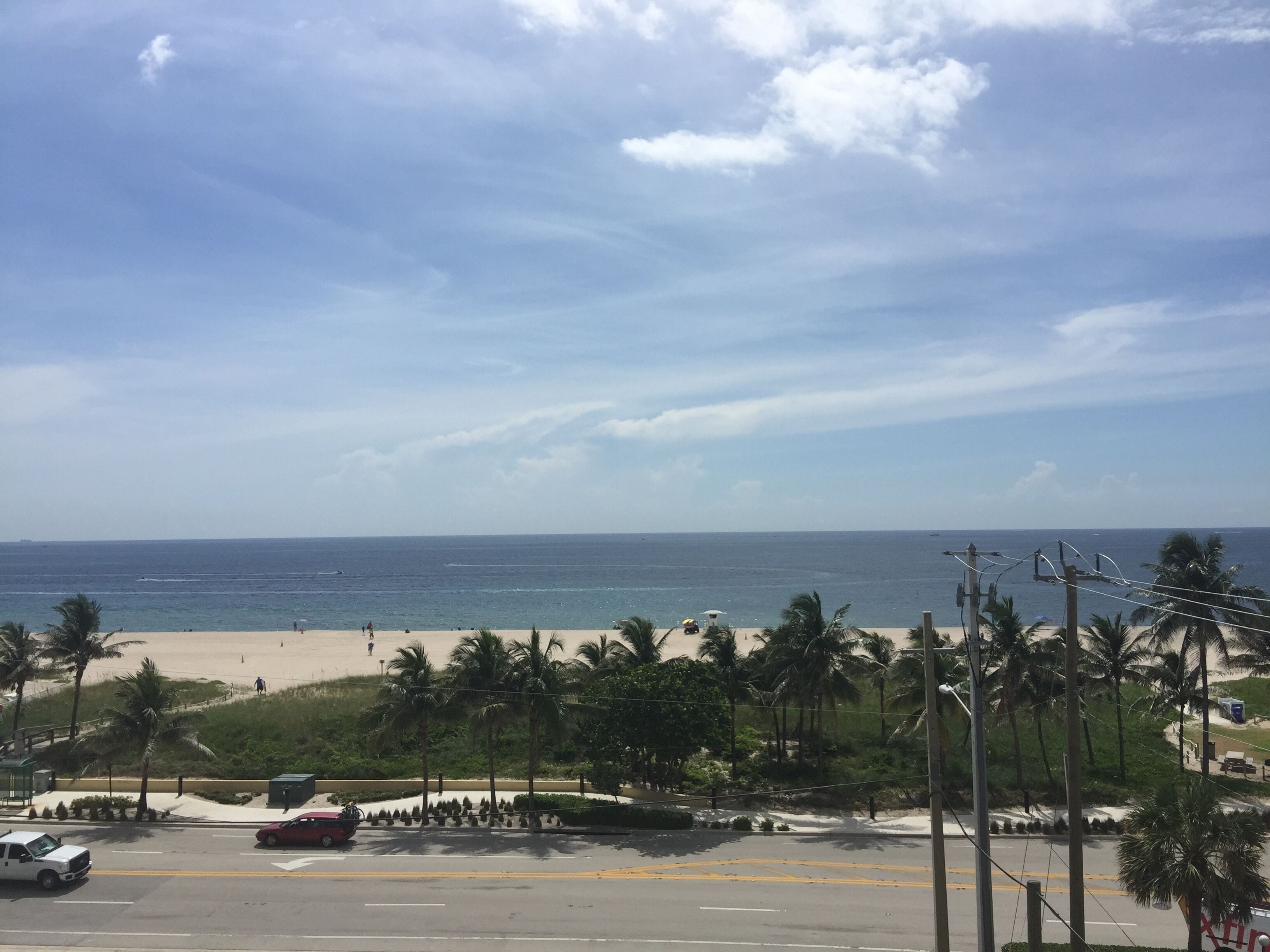 A coastal road with a beach in the background, palm trees, and a clear sky.