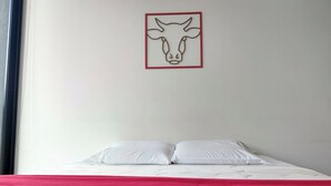 Ein Bett mit weißer Bettwäsche und einer roten Decke, ein weißes Kopfkissen sowie ein Wandbild mit einem Rindkopf.