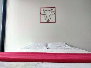 A bed with white bedding and a red blanket, a white pillow, and a wall-mounted artwork of a cow's head. - Modern apartment with a view of central Chapinero (Bogotá)