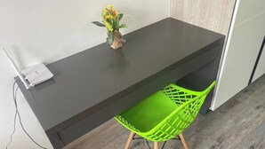 Ein modernes Zimmer mit einem dunklen Schreibtisch, einem grünen Stuhl und einer kleinen Vase mit Blumen darauf.