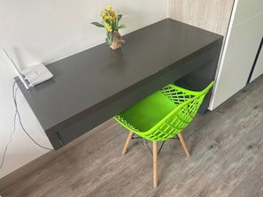 A modern room with a dark-colored desk, a green chair, and a small vase with flowers on the desk. - Modern apartment with a view of central Chapinero (Bogotá)