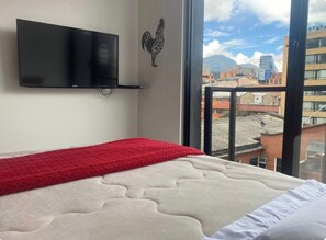 A hotel room with a bed, a television mounted on the wall, and a view of the cityscape through large windows. - Modern apartment with a view of central Chapinero (Bogotá)
