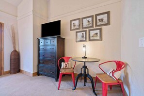 A room with a dark wooden cabinet, a round table with a lamp, and two red chairs. - Beaver Creek Penthouse | Resort Amenities & Views (Beaver Creek)