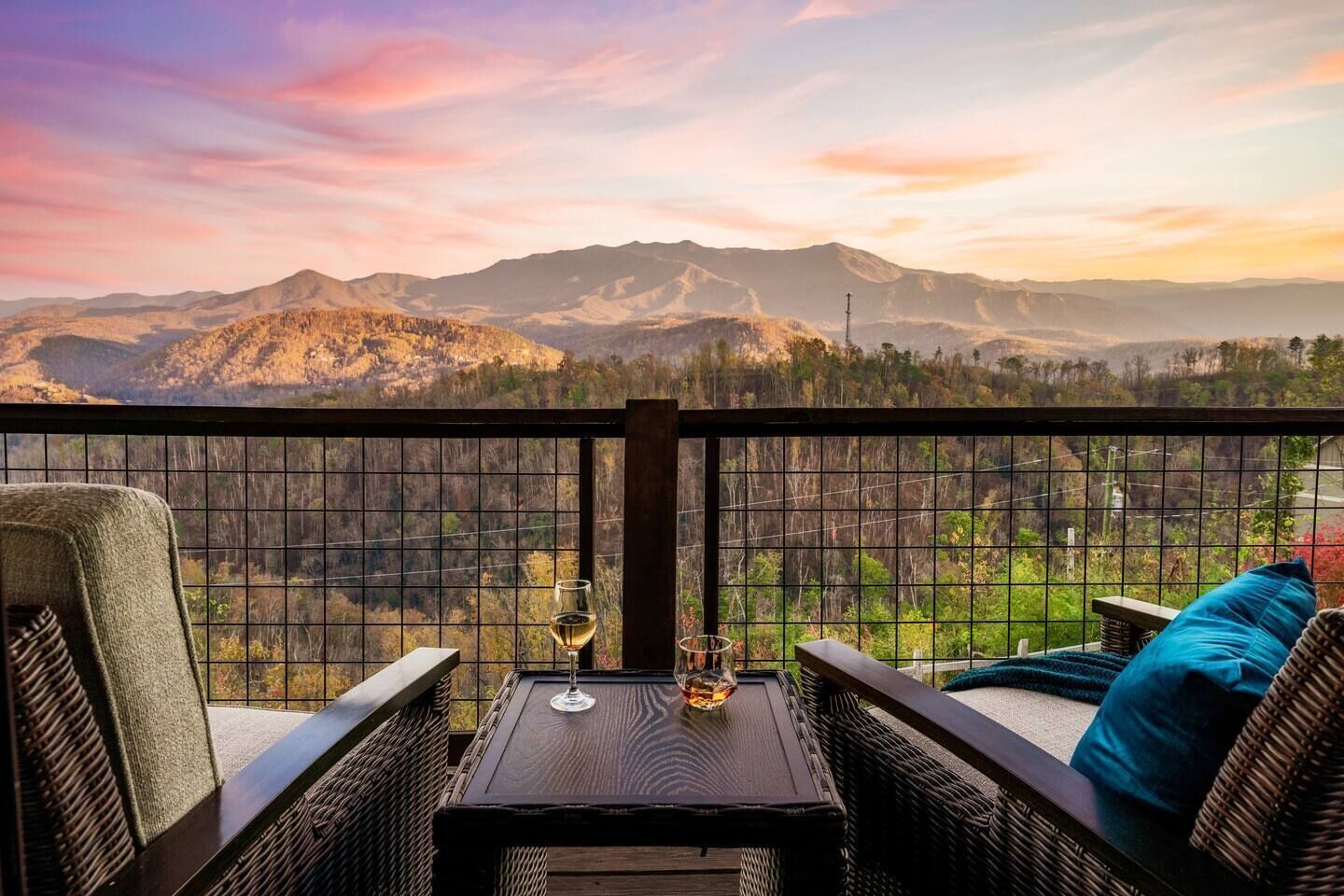 A balcony with wicker furniture, a glass of wine, and a view of mountains.