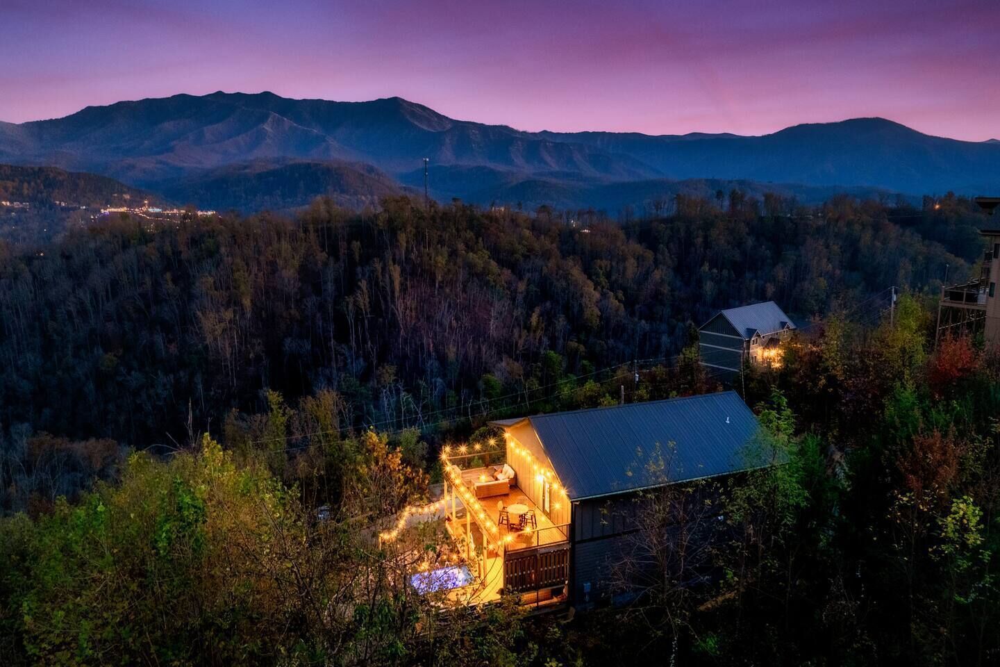 A rustic cabin with a porch and outdoor seating area, surrounded by forested mountains.