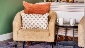 A cozy armchair with a patterned pillow, a small round table with a white mug, and a bed with striped bedding in a room with green walls. - Private Pool • Smoky Mountain Views • Game Room (Gatlinburg)