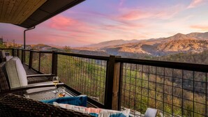 A balcony with wicker furniture and a glass table, overlooking a mountainous landscape. - Private Pool • Smoky Mountain Views • Game Room (Gatlinburg)