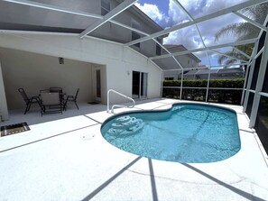 A swimming pool with a sunshade structure, a table with chairs, and a door leading to a covered area. - Golf Course Hideaway (Haines City)