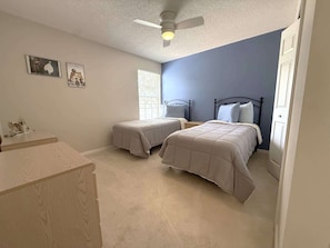 A bedroom with two beds, a ceiling fan, a window with blinds, and a door. - Golf Course Hideaway (Haines City)