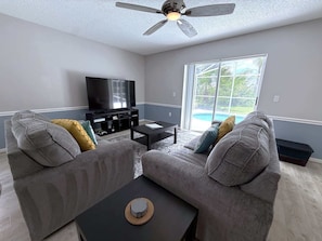 A living room with two grey sofas, a black coffee table, and a flat-screen TV. - Golf Course Hideaway (Haines City)