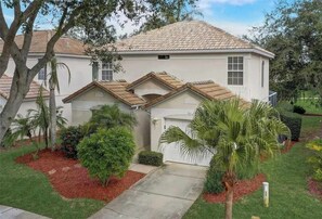 A two-story house with a tiled roof, a garage, and a well-maintained garden with various plants and a palm tree. - Golf Course Hideaway (Haines City)