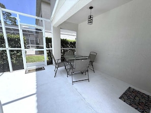A sunlit patio with a table and chairs, a glass door leading outside, and a hanging light fixture. - Golf Course Hideaway (Haines City)