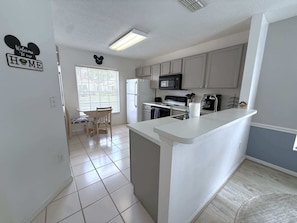 A modern kitchen with a central island, white cabinetry, and a dining area with a table and chairs. - Golf Course Hideaway (Haines City)