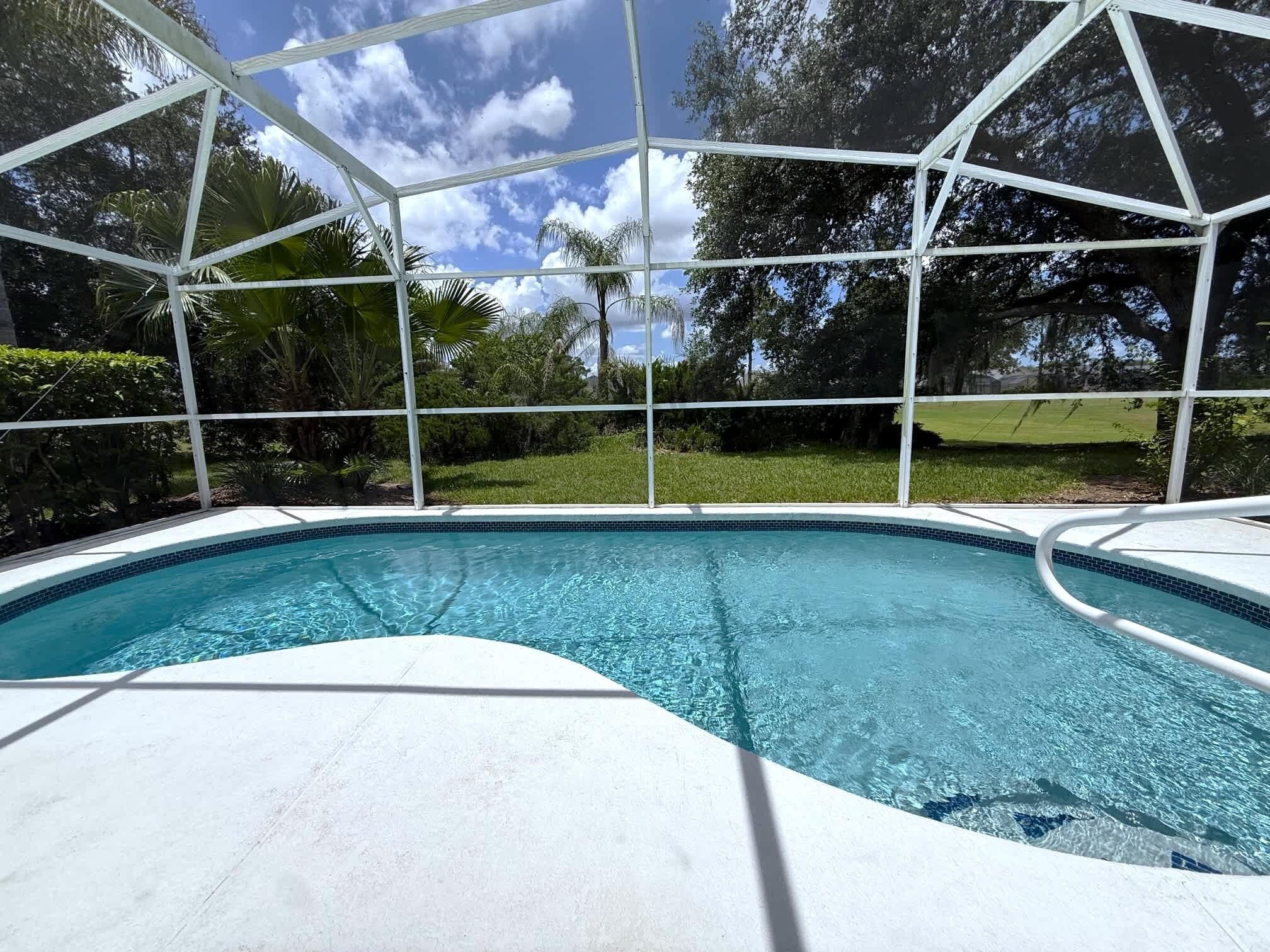 Una piscina con superficie de agua azul cristalina, rodeada por un deck blanco y una cerca de metal.