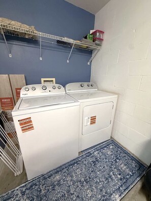 Una sala de bugaderia amb una rentadora i una assecadora Whirlpool, un estri de color blau i una prestatgeria amb diferents objectes.