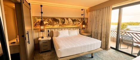 Habitación de hotel con una cama grande, una mesita de noche, una lámpara y vistas al exterior por una puerta corrediza.