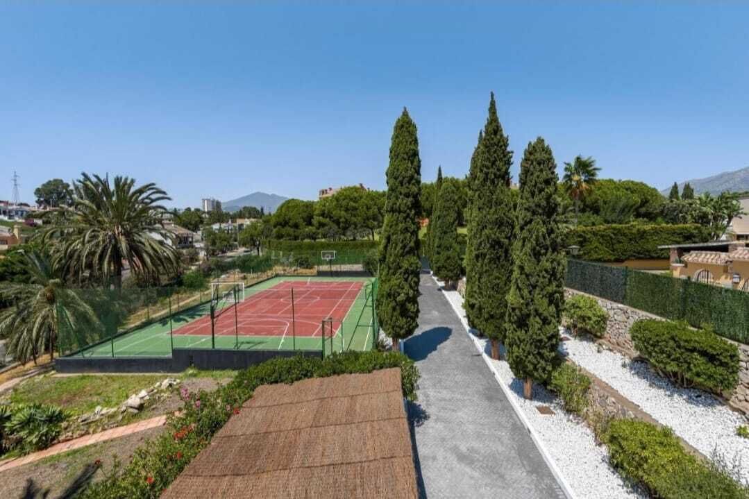 A tennis court surrounded by trees and a pathway.