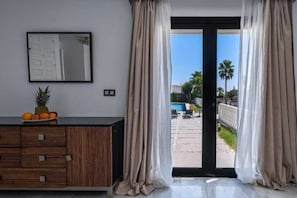 A room with a sliding glass door leading to an outdoor area, a wooden cabinet with drawers, a framed picture on the wall, and a fruit bowl on the cabinet.