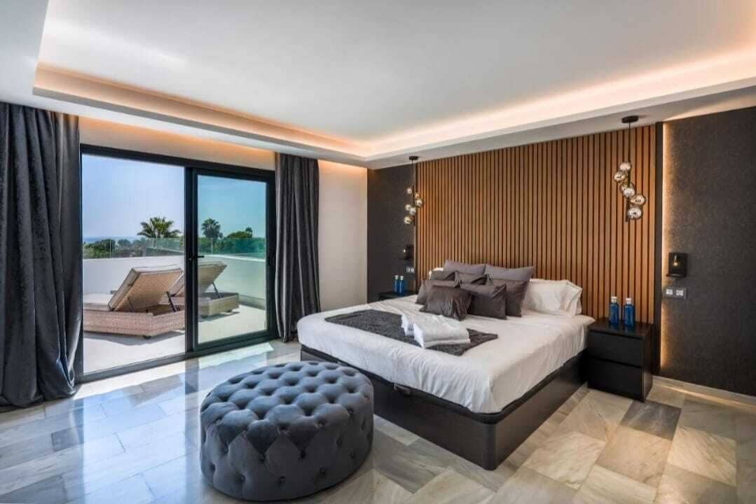 Een moderne slaapkamer met een groot bed, een zithoek met uitzicht en een schuifdeur naar buiten.