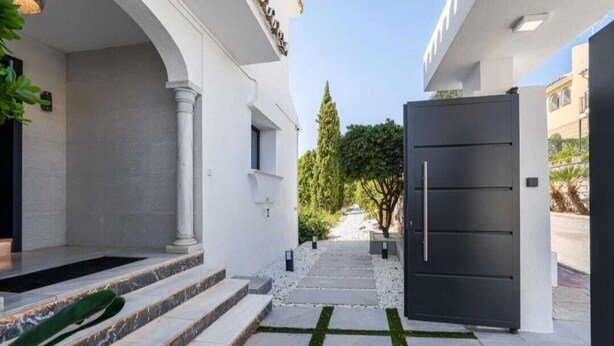 A modern entrance with a dark door, steps leading to a covered area, and a pathway with white pebbles.