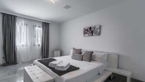 A modern bedroom with a large bed, a bedside table, a bench, and a wall-mounted artwork.