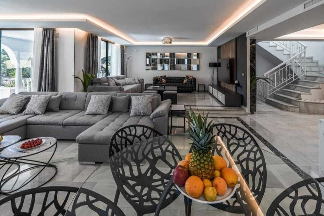 A modern living room with a sectional sofa, a dining table with chairs, and a fruit bowl.