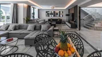 A modern living room with a sectional sofa, a dining table with chairs, and a fruit bowl.