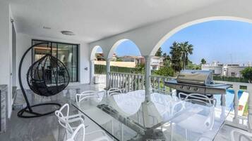 Un balcon avec une table et des chaises en verre, un fauteuil suspendu et un barbecue.