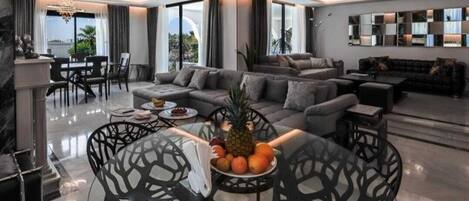 A modern living room with a sofa, dining table, and chairs. There is a fruit bowl on the table.