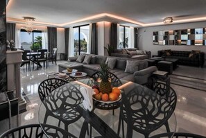 A modern living room with a sofa, dining table, and chairs. There is a fruit bowl on the table.