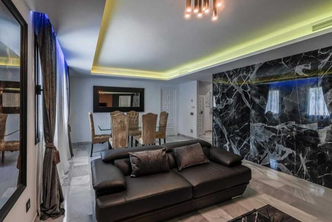 Een moderne woonkamer met een modulaire bank, een eetgedeelte met stoelen en een grote marmeren wand.