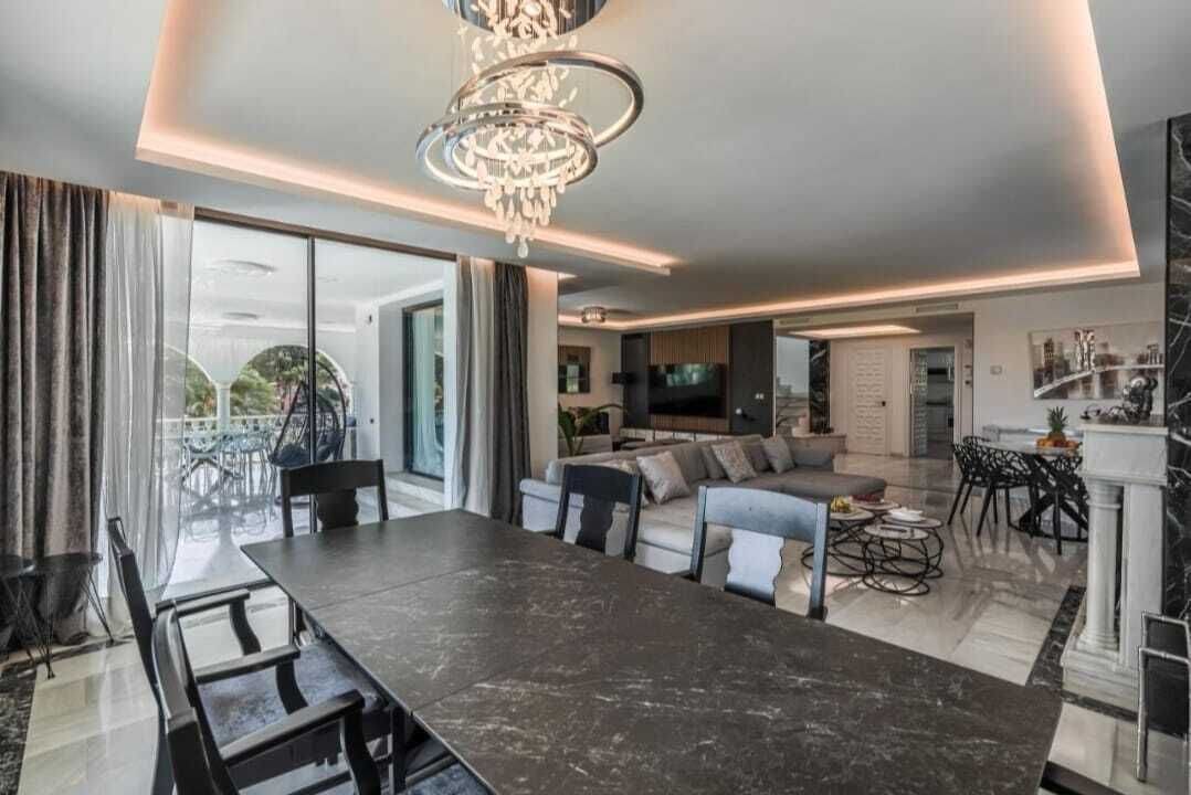 A modern living room with a dining area, a chandelier, and a television.