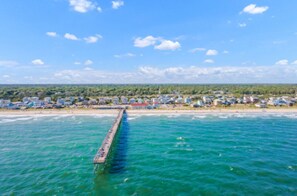 Eine Küstenstadt mit einem Steg, der sich ins Meer erstreckt, umgeben von Wohnhäusern und viel Grün.