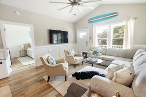 Ein Wohnzimmer mit Deckenventilator, einer Couch, Sesseln, einem Couchtisch und einem Fernseher.