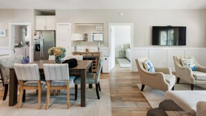 A modern living room with a dining area, a kitchen, and a TV mounted on the wall. - Charming Oak Island Retreat — Minutes from the Beach with Private Hot Tub (Oak Island)