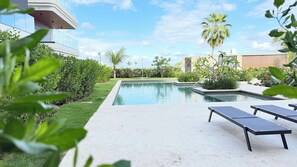 Ein Swimmingpool mit Liegestühlen, umgeben von Grünflächen und modernen Gebäuden.