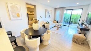 A modern living room with a dining area, a sofa set, and a large window with a view of greenery. - Vermare Bliss 2 Br private pool BBQ Cap Cana (Punta Cana)