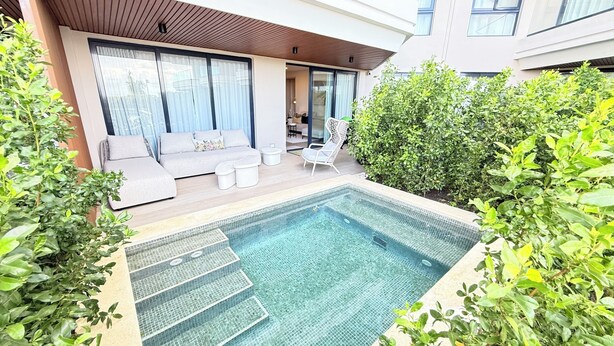 Un espace piscine extérieur moderne, doté d’un canapé et de chaises longues, le tout entouré de verdure.