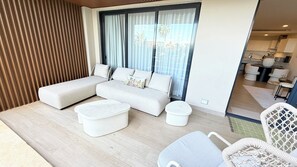 Ein moderner Wohnbereich mit Sofa, Hocker und Sessel, einem Esstisch und einer durch eine Glastür einsehbarer Küche.