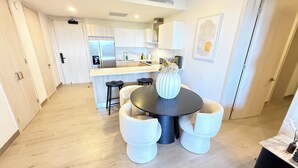 A modern kitchen with white cabinets, a central island, and a dining area with a round table and white chairs. - Vermare Bliss 2 Br private pool BBQ Cap Cana (Punta Cana)
