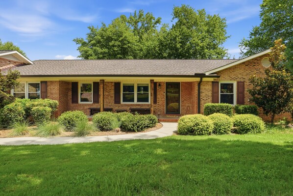 A two-story brick house with a front porch, a covered patio, and a well-maintained lawn.