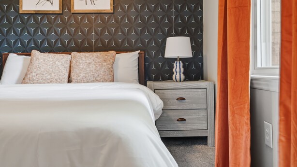 A neatly made bed with white linens and multiple pillows, a bedside table with a lamp, and a geometric patterned wall. - 4Br Lux Stay w/Pool & Game Room - Sleeps 10 (Concord)