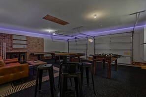 A room with a foosball table, a pool table, a brick wall, and a garage door.
