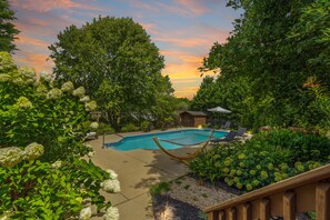 A pool area with a hammock, lounge chairs, and a wooden deck.