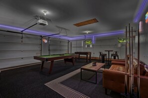 Ein Billardtisch in einem Raum mit Projektor an der Decke und stimmungsvoller Beleuchtung.