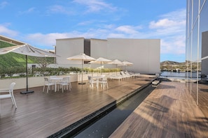 A rooftop terrace with outdoor seating, a pool, and a modern building in the background. - New Cabo Golf Retreat w/ Water Mirror Views (San José del Cabo)