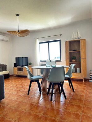Una sala de estar moderna con comedor, televisor y un amplio ventanal.