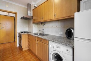 A kitchen with wooden cabinets, a built-in oven, a washing machine, and a microwave.